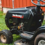 Close-up of a black riding lawn mower parked on a lawn next to a red building.