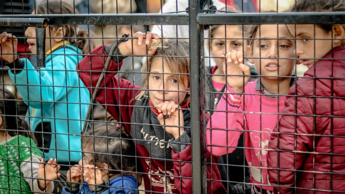 A poignant image of children behind a metal fence in Idlib, Syria, highlighting togetherness and diversity.