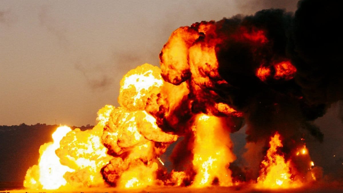 A powerful explosion with intense flames and dark smoke creating a dramatic outdoor scene during daytime.