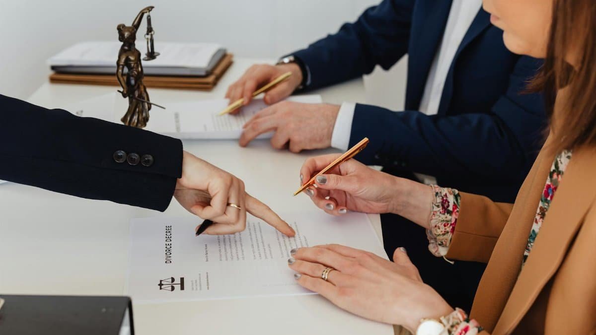 Hands signing a divorce decree, with a justice statue nearby, symbolizing legal proceedings.