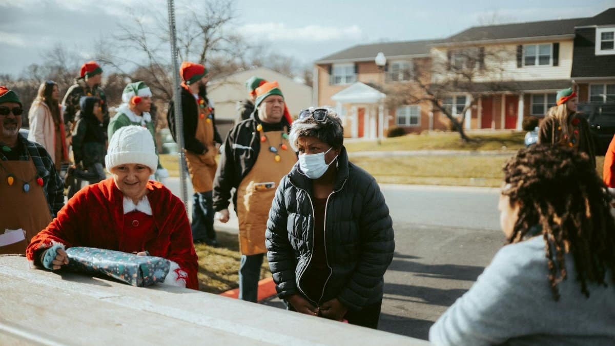 A neighborhood holiday gathering featuring adults dressed in elf costumes distributing gifts on a street.