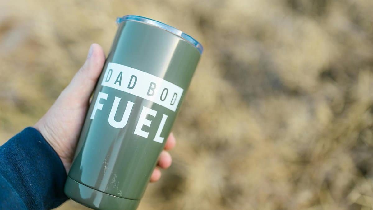 Green tumbler with 'Dad Bod Fuel' text held outdoors. Perfect for coffee or tea lovers.