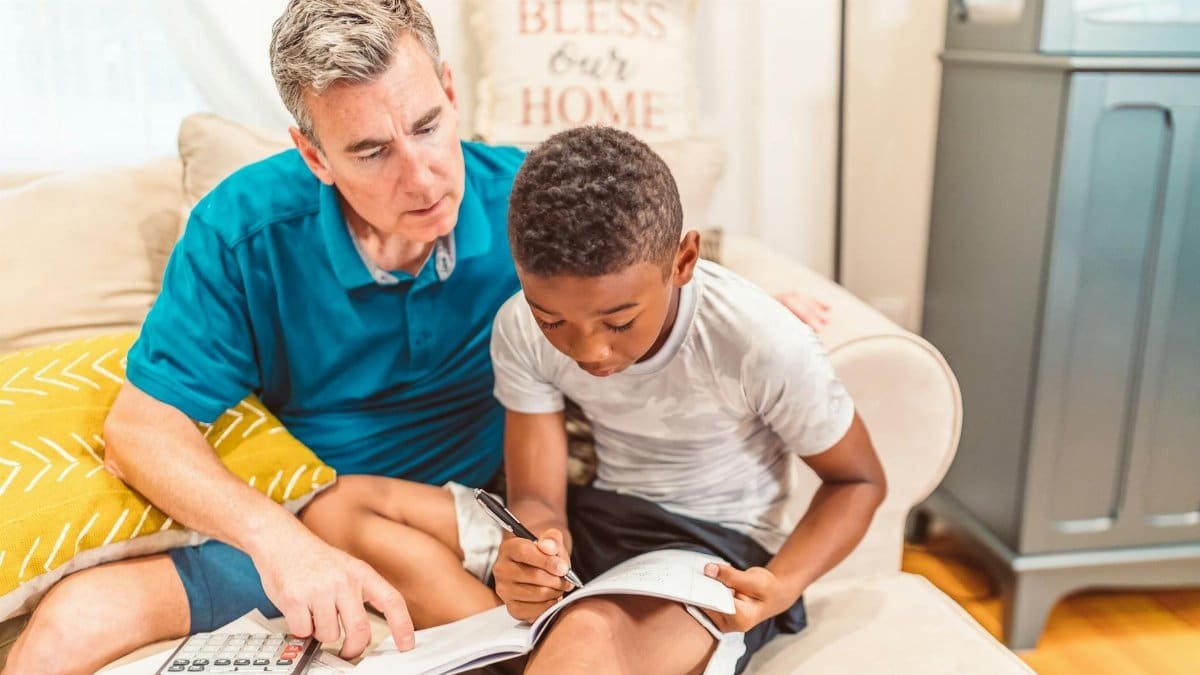Father and son studying together at home, focused on homework with textbook and calculator.