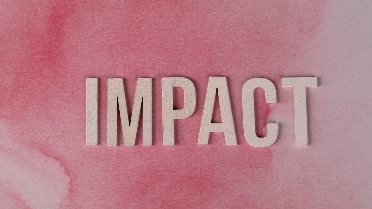 Wooden letters spelling 'IMPACT' against a textured pink watercolor backdrop, symbolizing influence and change.