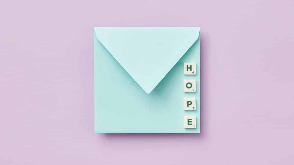 A minimalist envelope paired with Scrabble tiles spelling 'HOPE' against a pastel backdrop.