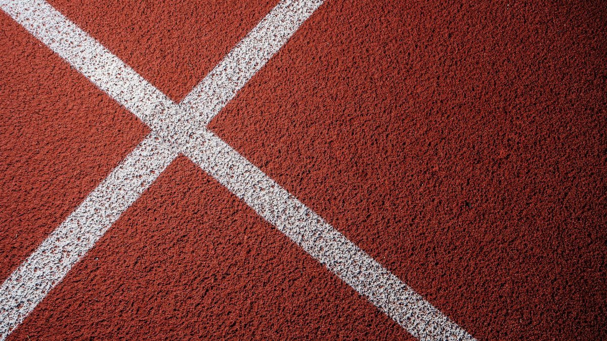Detailed close-up of white intersecting lines on a red athletic track surface, ideal for sports themes.
