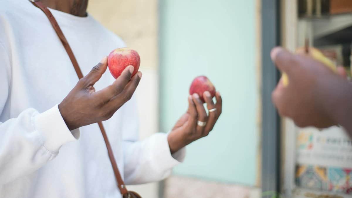 A person holding apples outside a store, demonstrating outdoor shopping.
