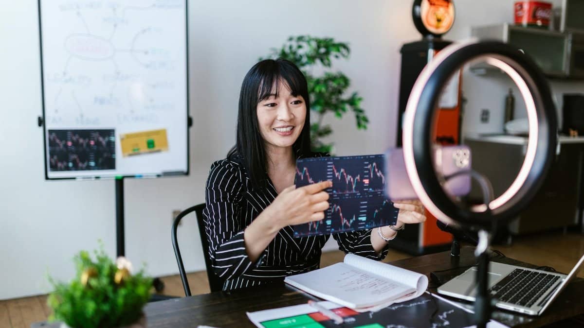 Asian woman discussing cryptocurrency investment during a vlogging session with charts.