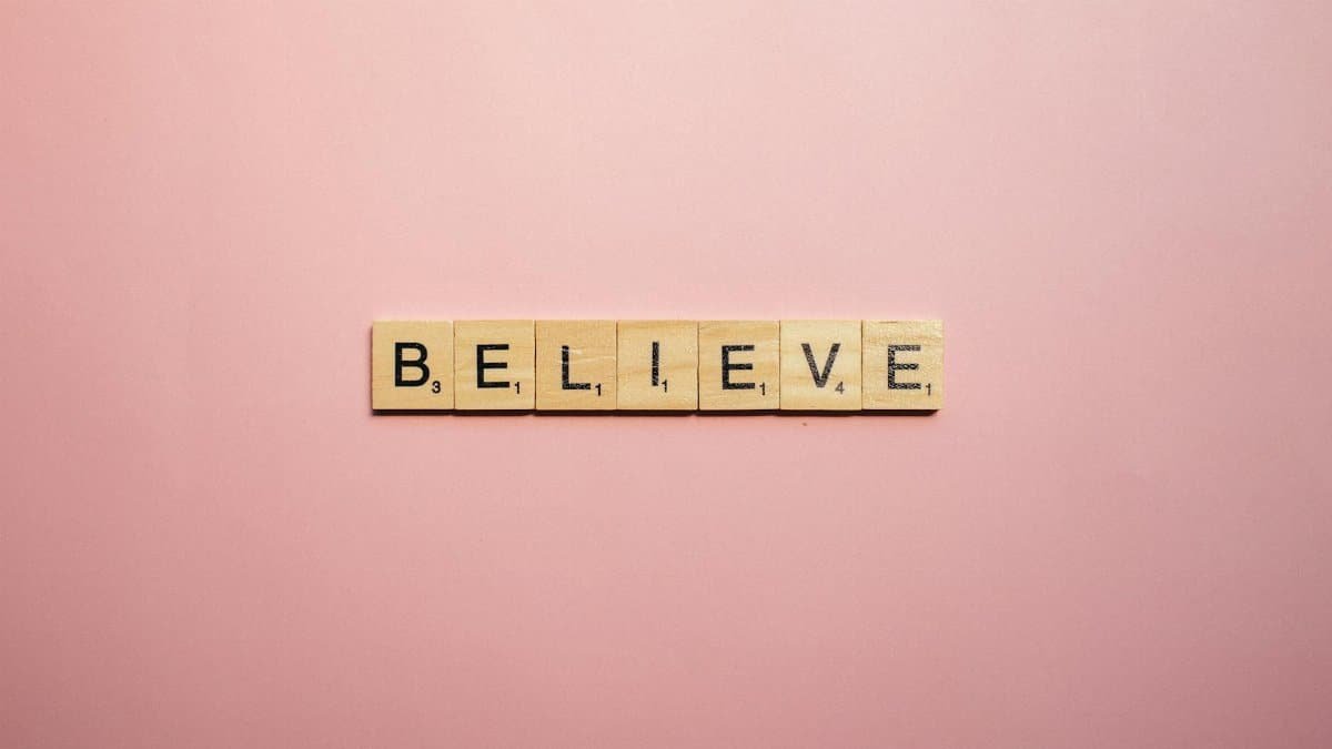 Wooden letter tiles spell 'Believe' on a soft pink background, inspiring positivity.