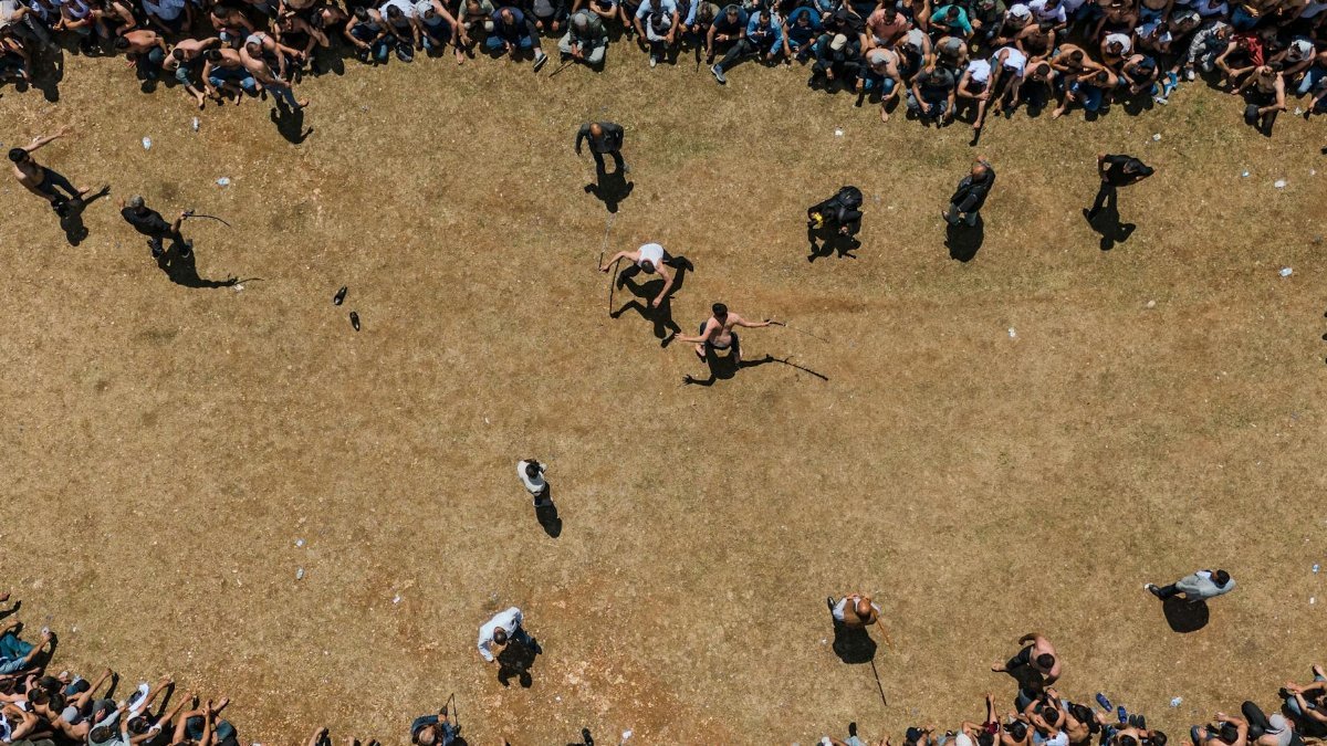 Aerial view of a large crowd surrounding an open field event with spectators watching closely.