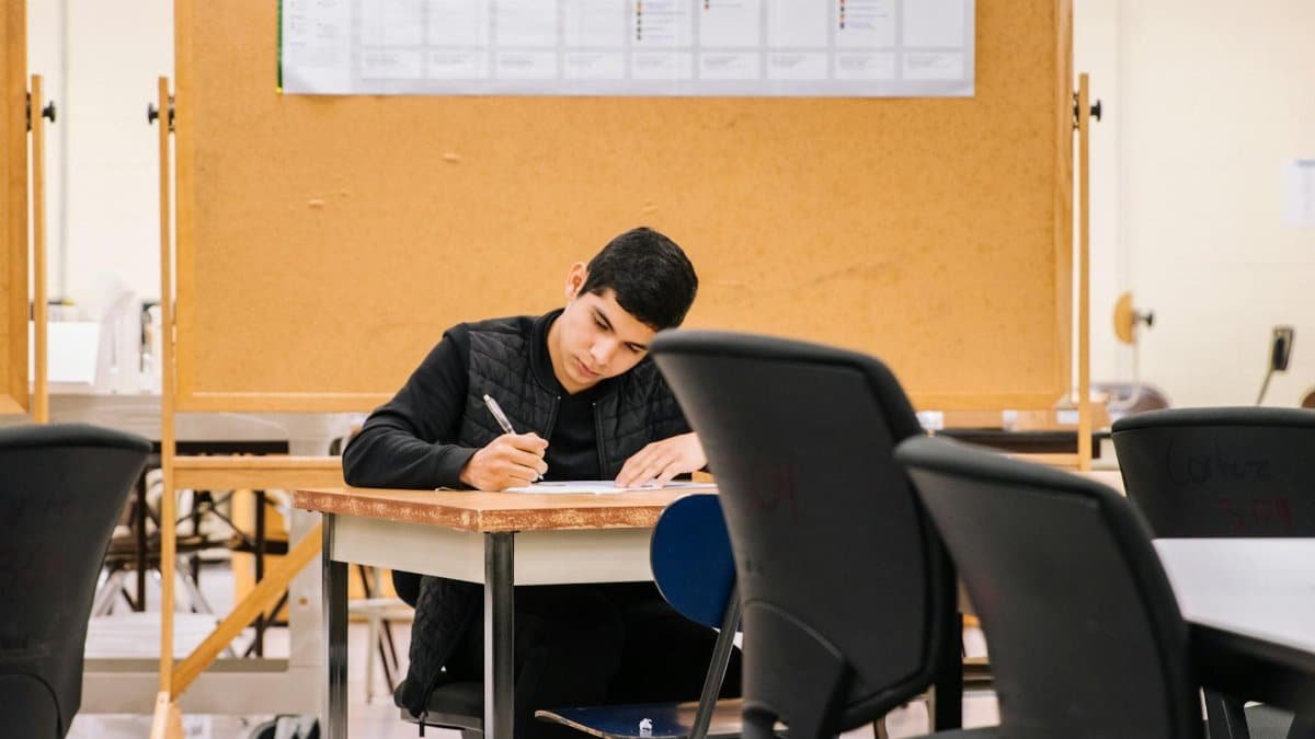 Young man focused on writing in a classroom, ideal for education concepts.