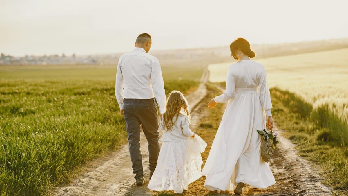 A family of three walks down a country road in summer, capturing a serene moment of togetherness.