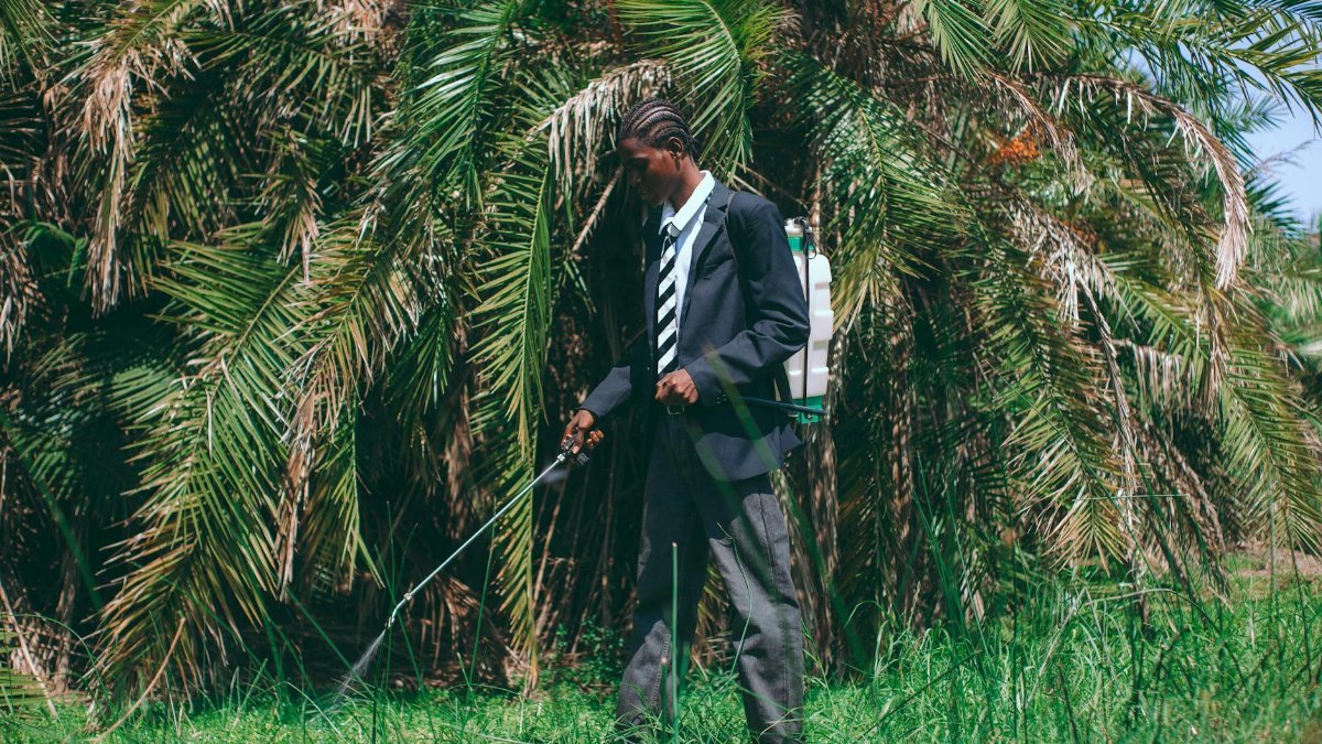 A man in a suit uses a sprayer in a lush garden setting in Accra, Ghana.