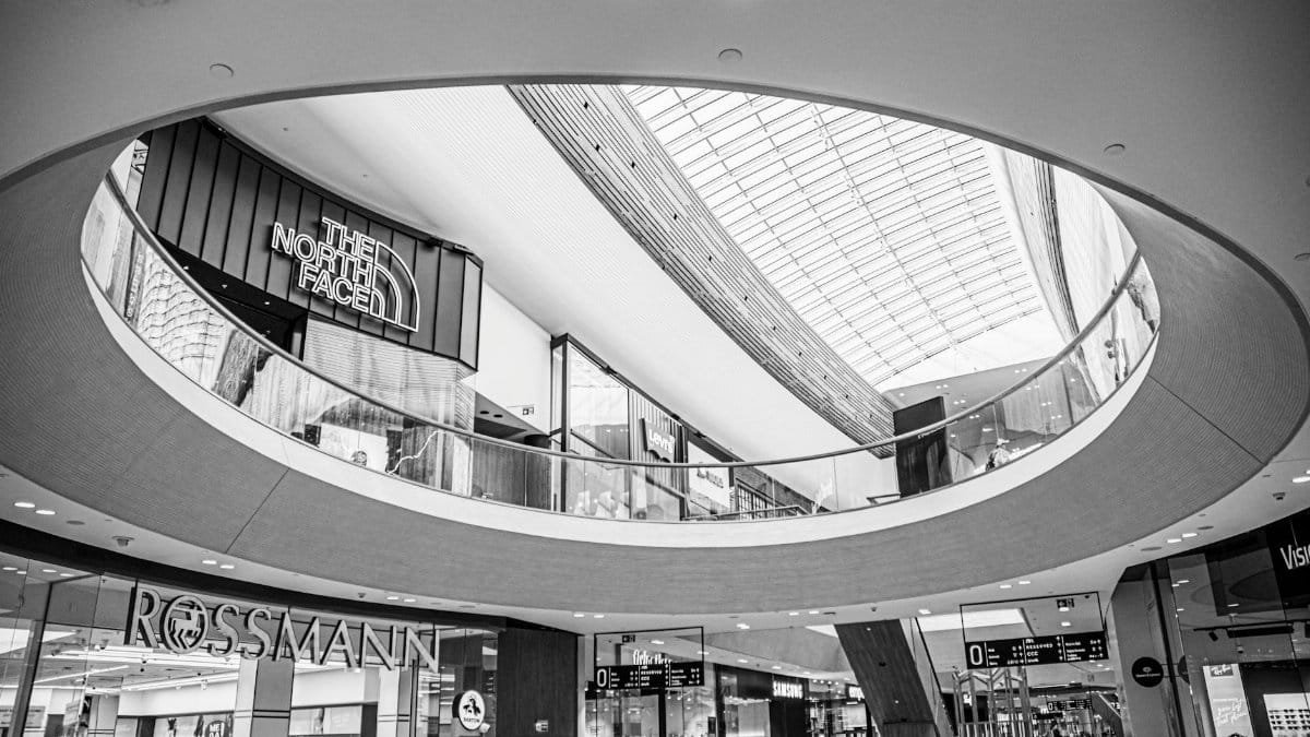 Black and white image showcasing the modern interior design of a shopping mall with prominent brand displays.