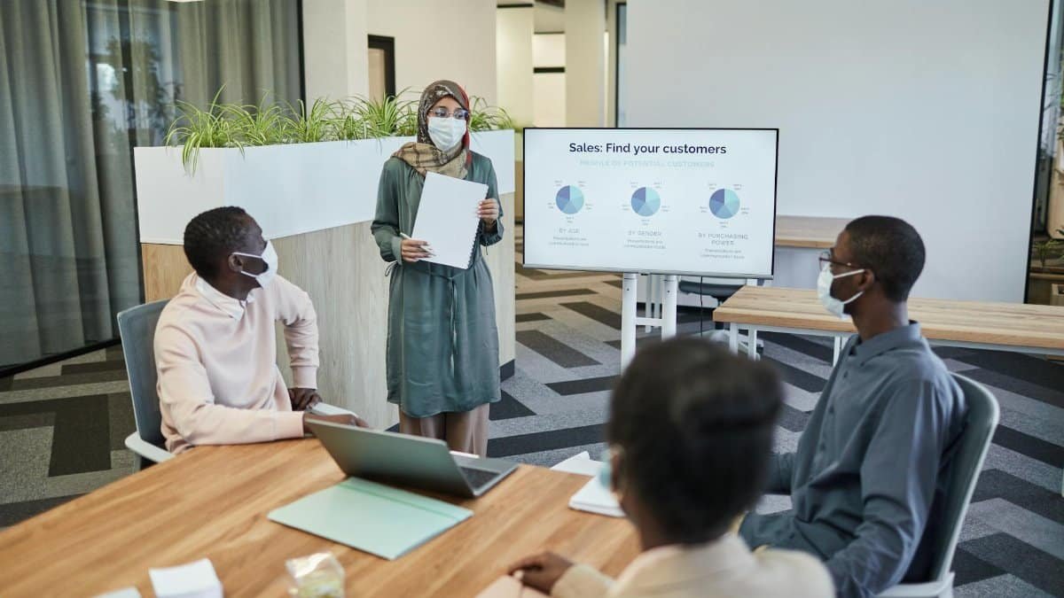 Colleagues wearing masks in a modern office discussing sales strategies.