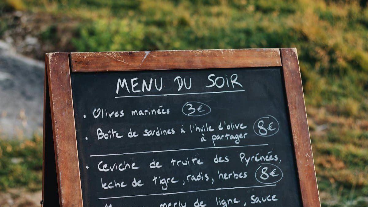 Chalkboard menu stand listing French dishes and prices in an outdoor setting.
