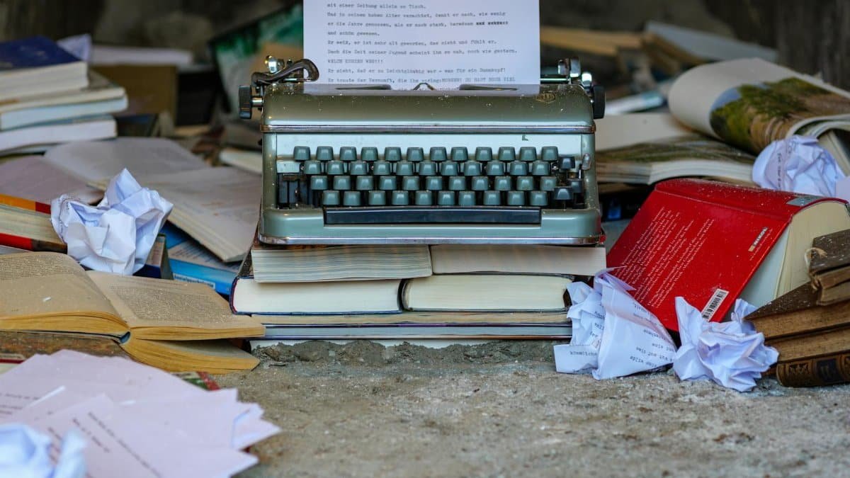 A vintage typewriter surrounded by open books and crumpled papers, symbolizing creative chaos.