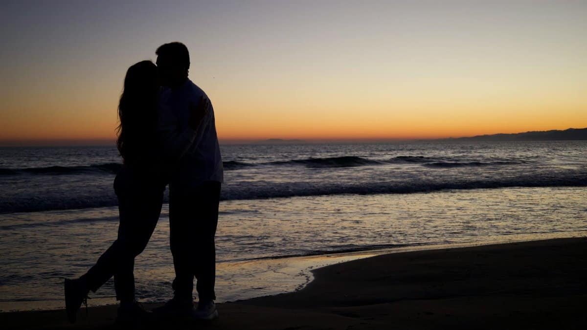 Silhouette of a couple embracing on a beach during sunset, capturing a romantic moment.