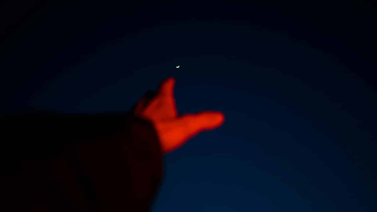 Blurred hand reaching towards a crescent moon in a dark night sky, capturing a sense of aspiration.