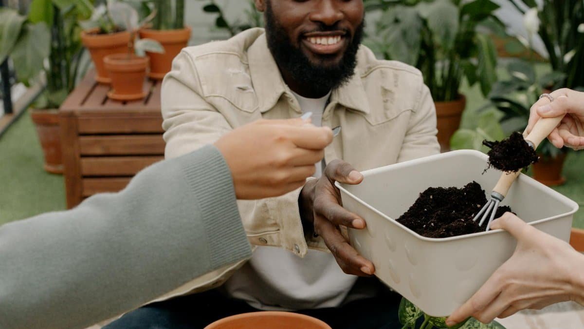 A joyful man shares a gardening moment with friends, tending to plants indoors.