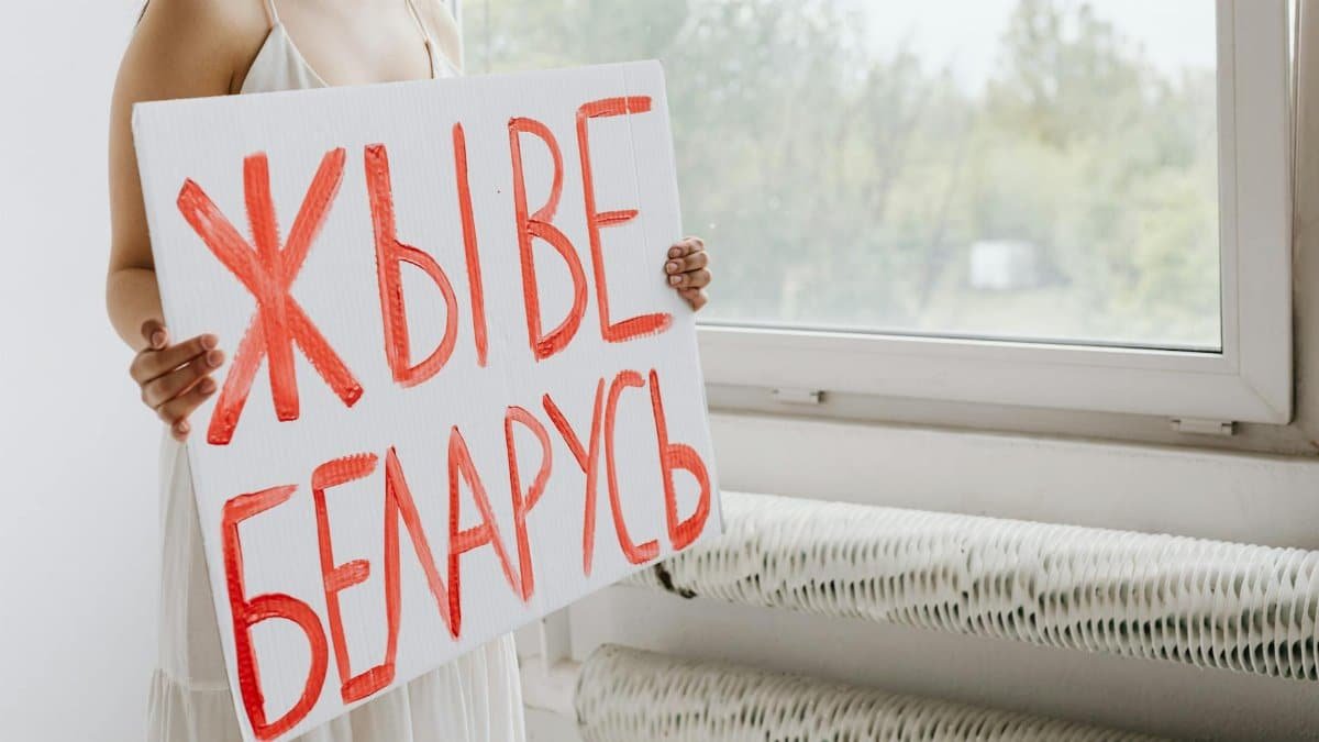 A woman holds a Belarusian sign near a window, symbolizing activism.