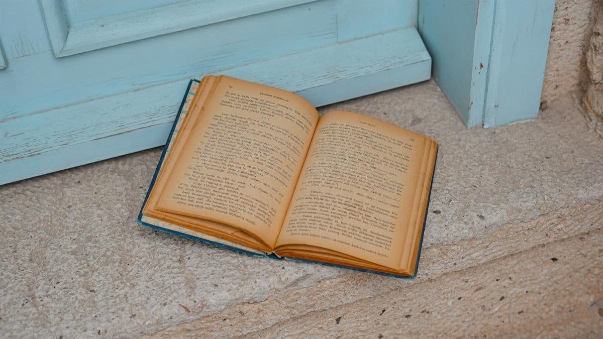 An open vintage book resting on stone steps by a light blue door.