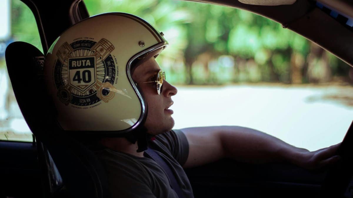 Man wearing a Ruta 40 helmet driving a car, looking into the distance.