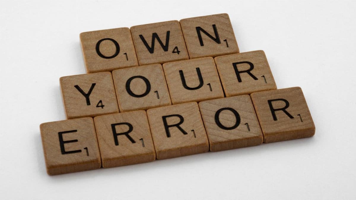 Scrabble tiles forming the phrase 'OWN YOUR ERROR'. Great for concepts of accountability and motivation.