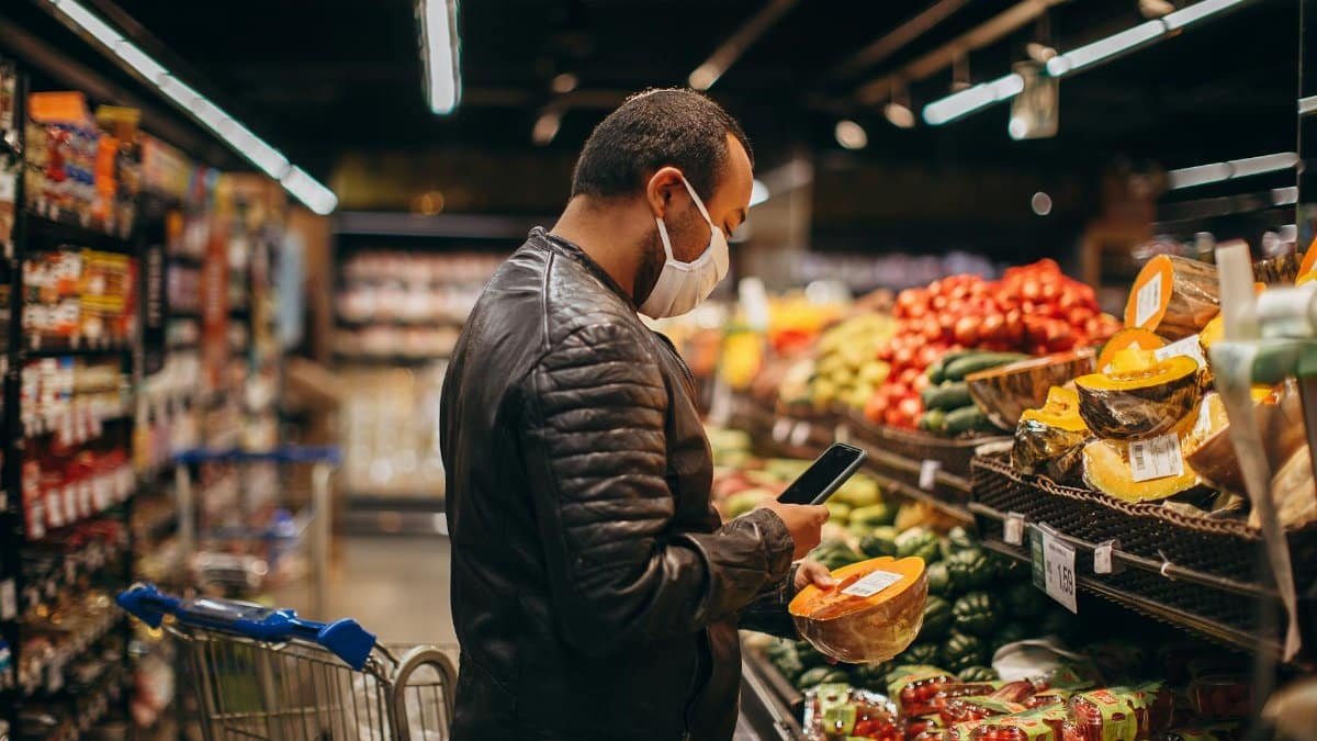 Man shopping in grocery store, inspecting fresh produce while wearing a mask.