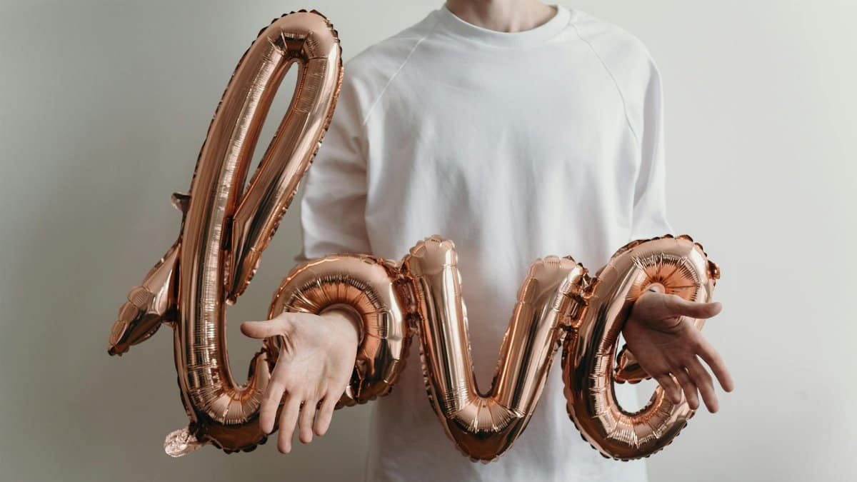 A man holding rose gold love balloons wearing a white t-shirt, showcasing minimalist love symbolism.