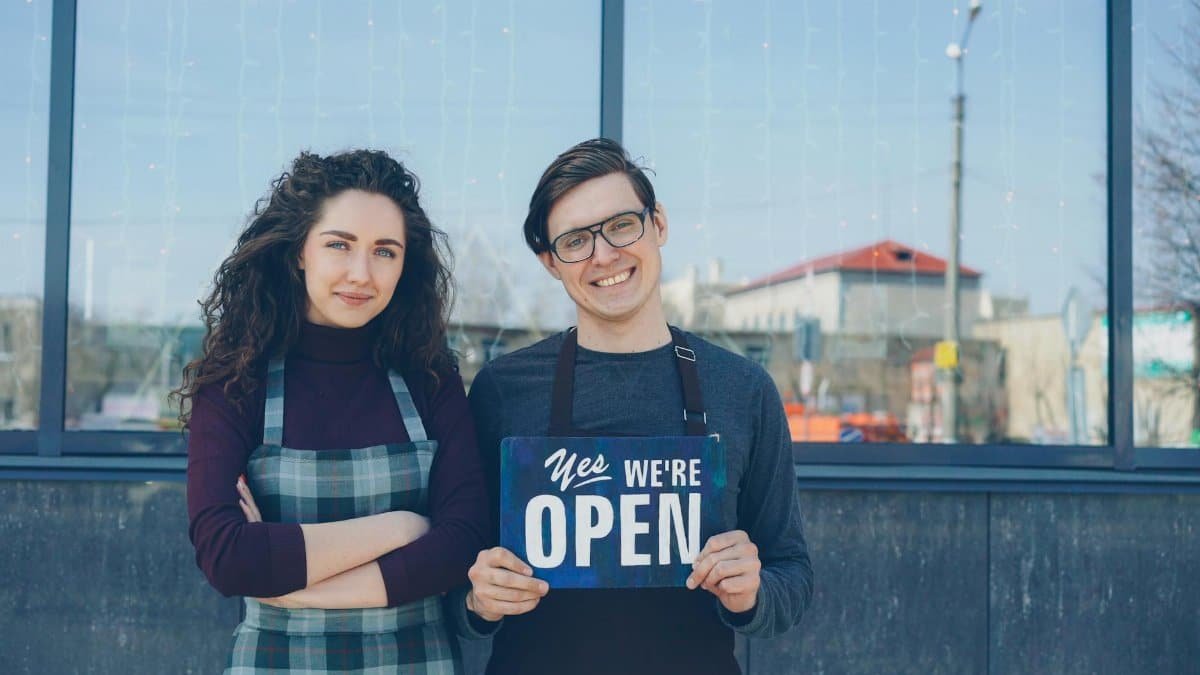 Two cafe owners proudly holding an open sign outside their storefront.