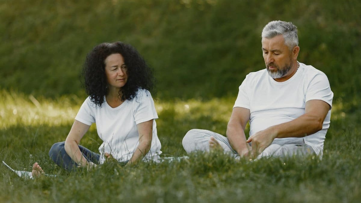 A middle-aged couple enjoying a peaceful day sitting on grass in the park under the sun.