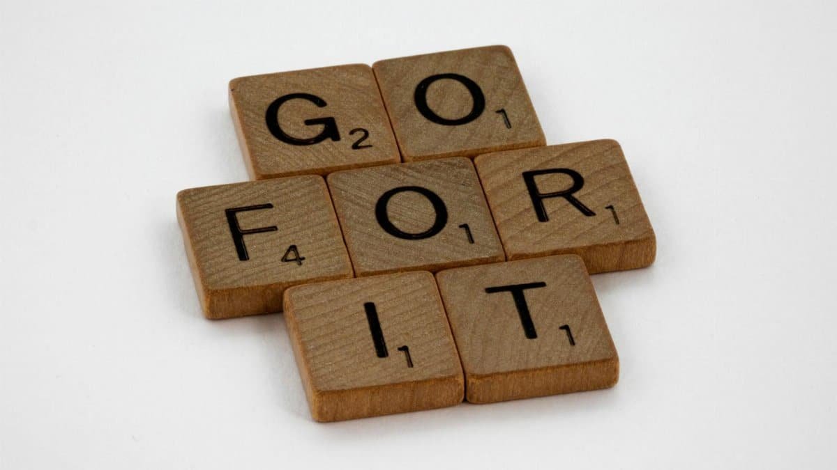 Close-up of Scrabble letters forming the phrase 'Go For It' on a white background.