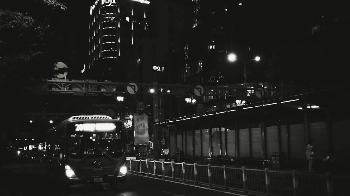 Black and white capture of a city street at night with a bus and illuminated buildings.