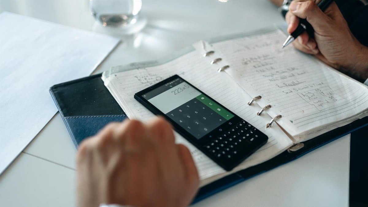 Close-up of hands writing in notebook with smartphone calculator on the table.
