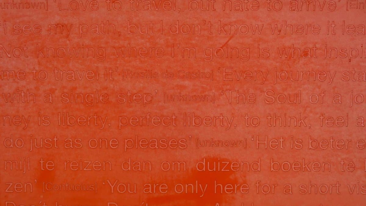 Detailed close-up of engraved text featuring inspirational travel quotes on a red surface.
