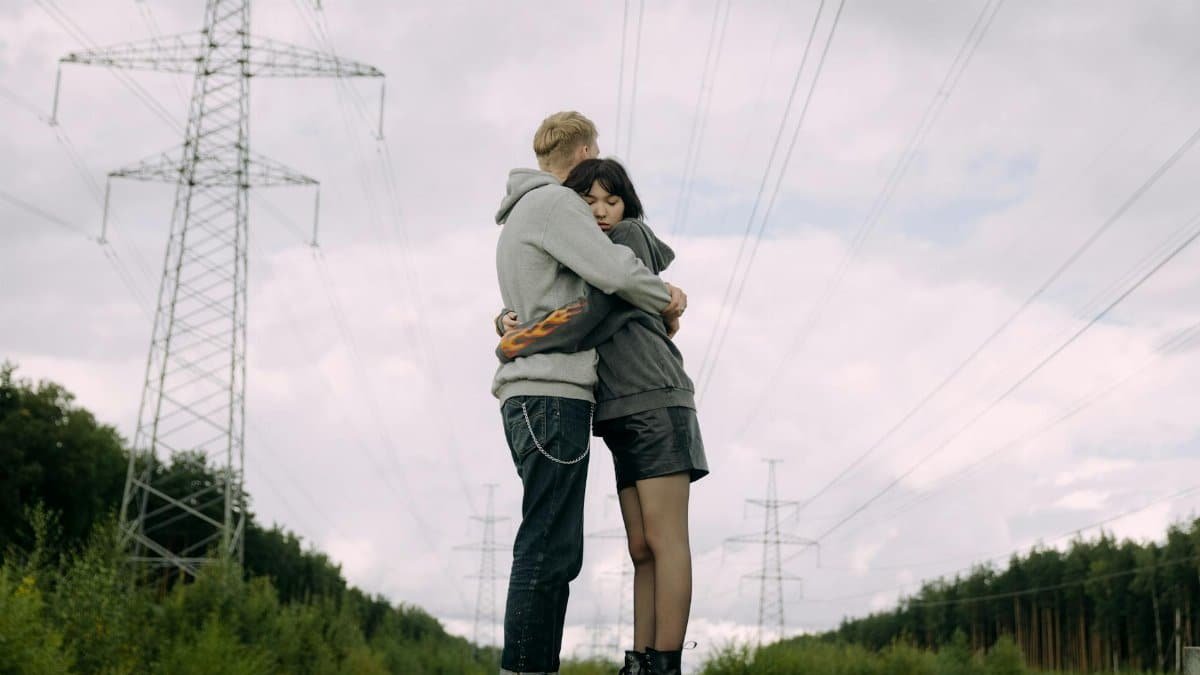 A couple shares a tender hug outdoors beneath towering power lines on a cloudy day.