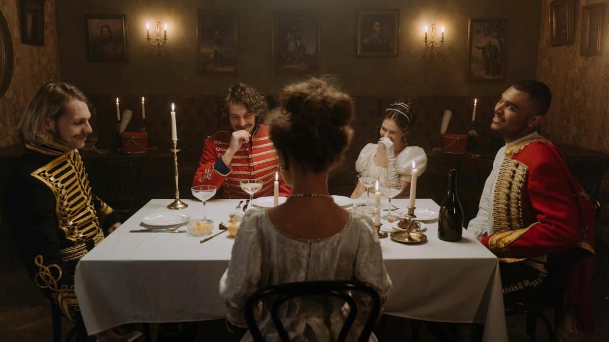 A group in period costumes enjoying a candlelit dinner in an opulent dining room.