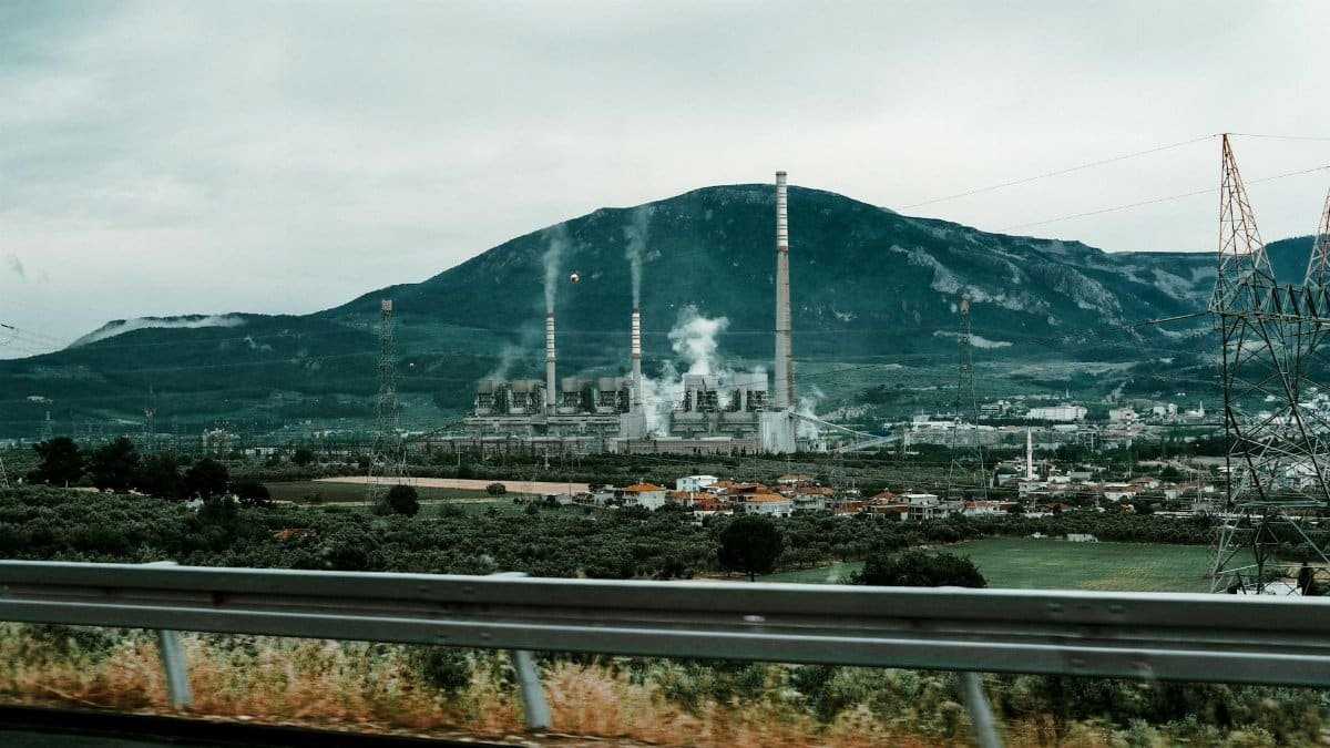 Power plant in a mountainous landscape with smokestacks emitting smoke, highlighting industrial impact on the environment.