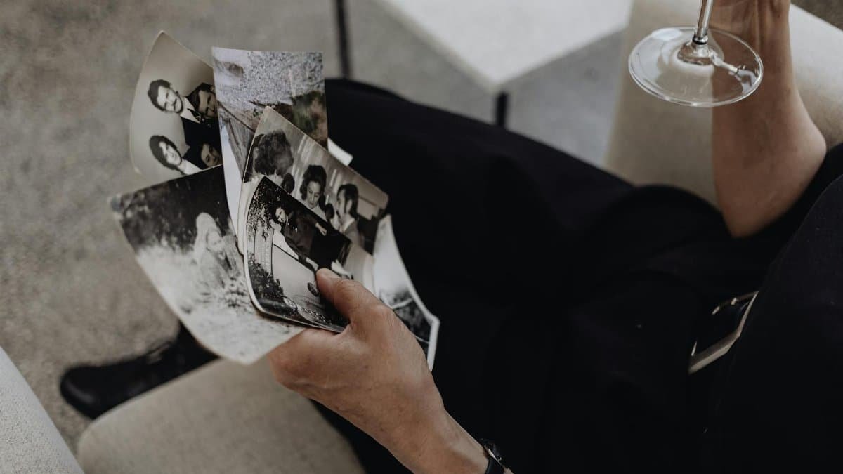 A person reflecting on memories while holding photographs and a wine glass.