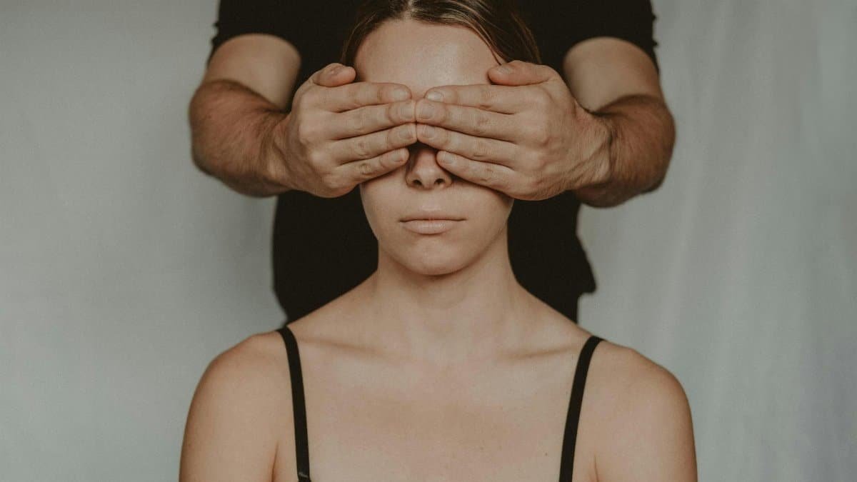 Faceless man covering face with hands of anonymous female while standing behind back in room on white background in flat