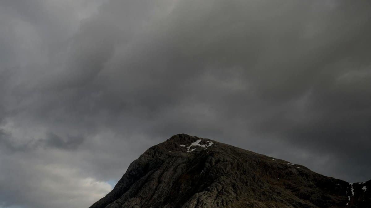 A rugged mountain peak beneath a dark, cloudy sky captures a dramatic and moody atmosphere.