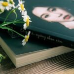 Close-up of a book with chamomile flowers on a wooden surface, conveying a peaceful reading atmosphere.