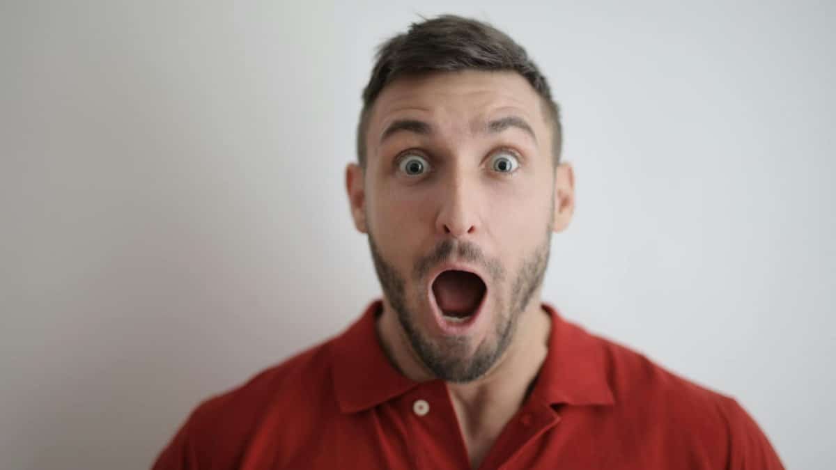 Portrait of a shocked man in a red polo shirt with a white background, expressing surprise.