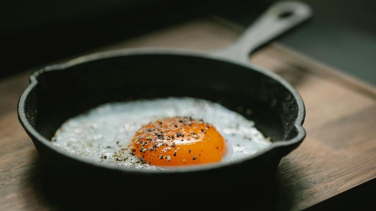 High angle of pan with fried egg with seasoning placed on wooden board in kitchen