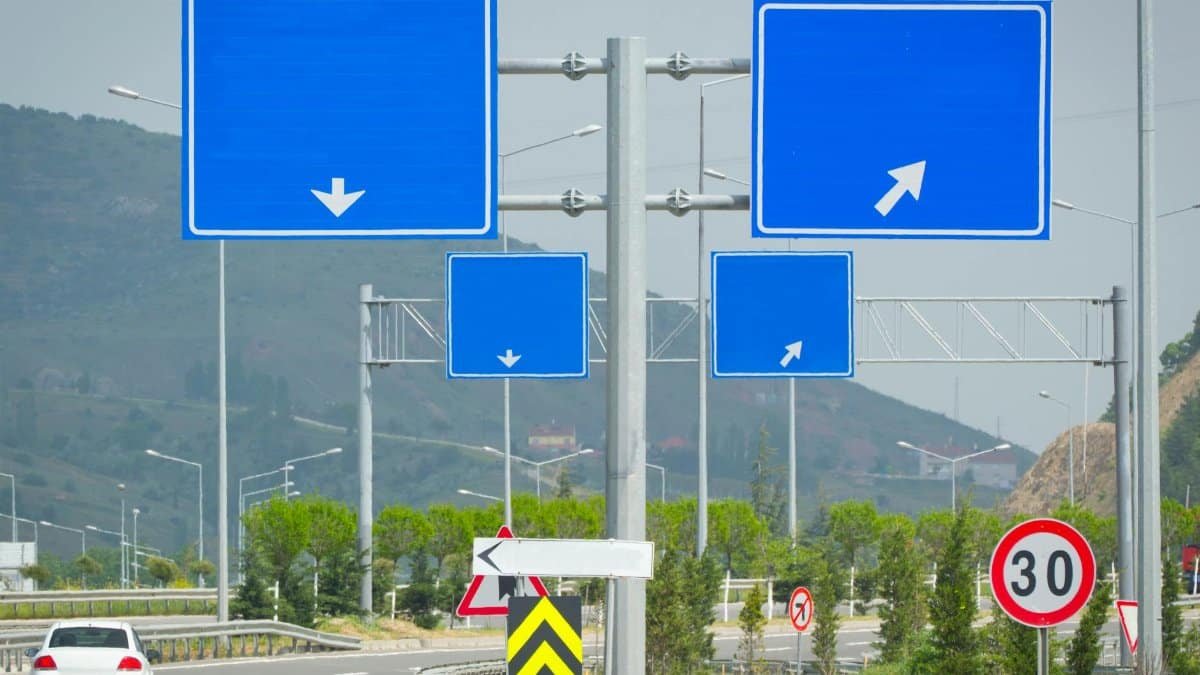 Series of blank blue road signs with arrows on a highway intersection and speed limit in scenic outdoor setting.