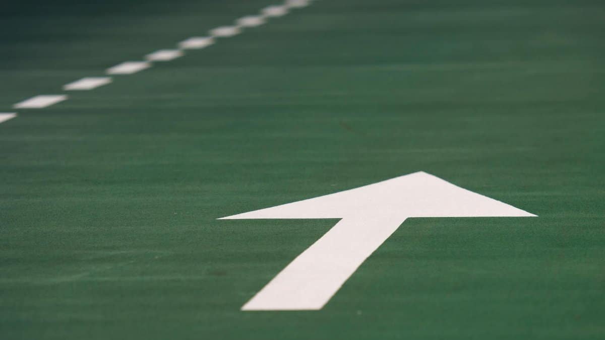 Close-up of a white arrow on a green road surface indicating direction.