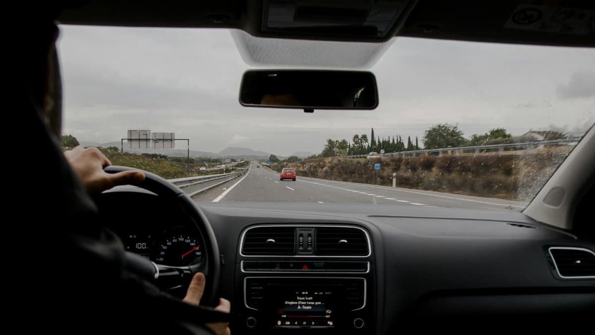 Anonymous man driving fast along asphalt road on modern vehicle in overcast weather