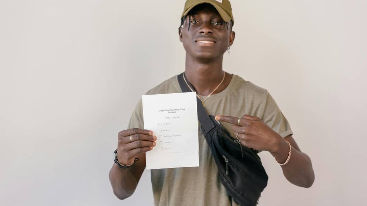 Young adult smiling and pointing at electoral ballot paper, emphasizing the importance of voting.