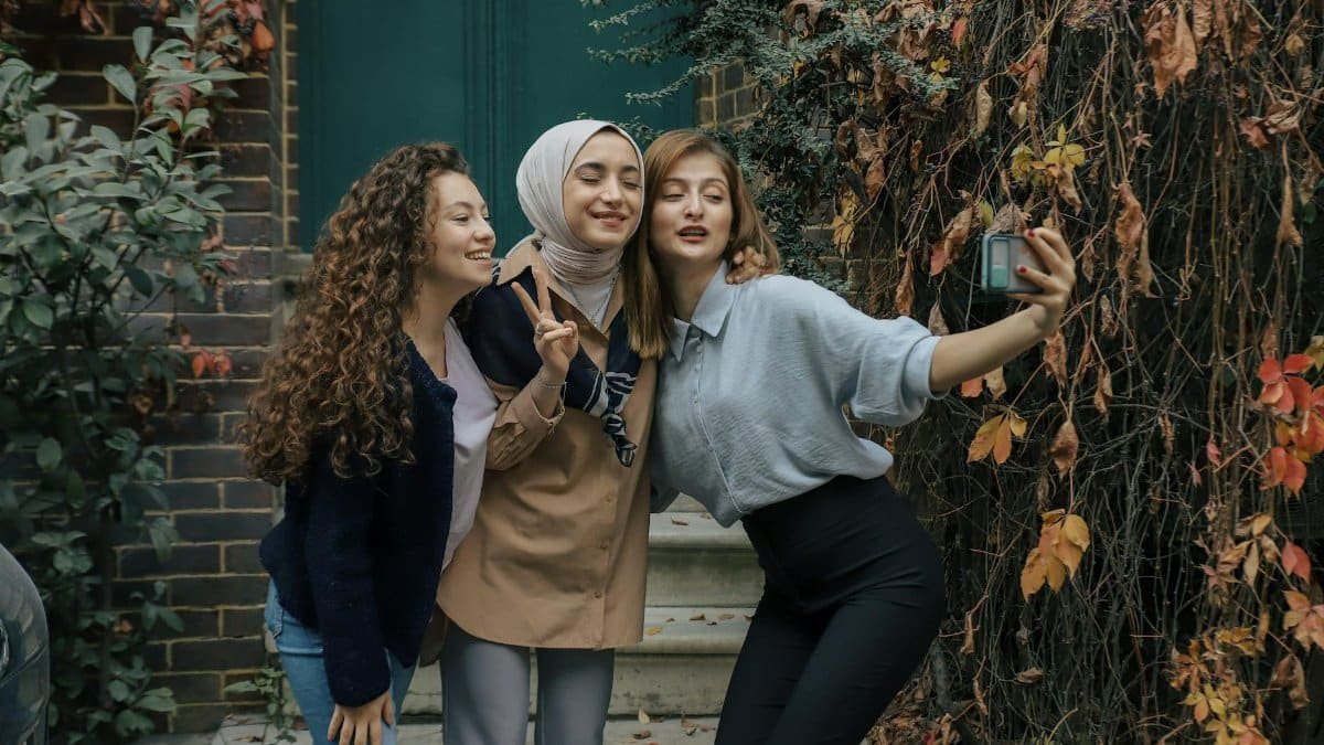 Three women smiling and taking a selfie outdoors in İstanbul, Türkiye, with autumn foliage.